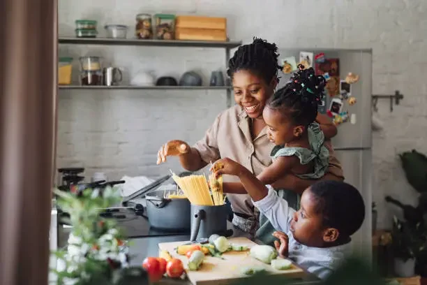 Mother cooking pasta with her two young children in a home kitchen