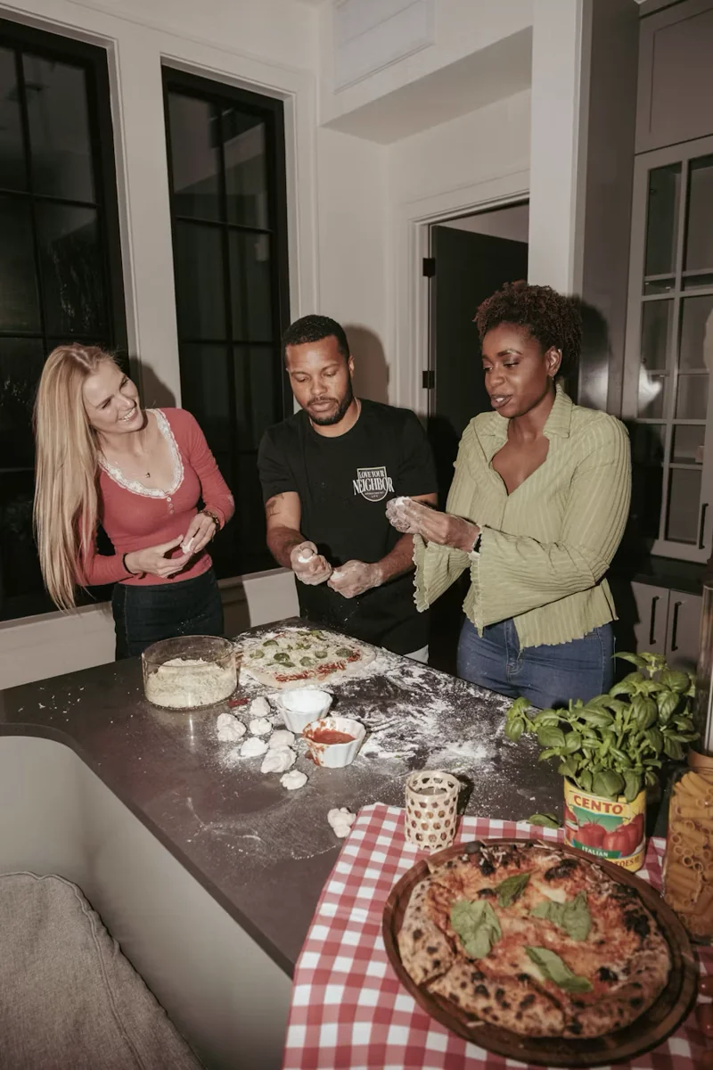 Three friends making pizza together at a kitchen counter